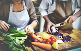 A couple cuts vegetables while preparing a healthy meal.