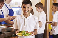 A young boy gets a plate including healthy fruits and vegetables from a school cafeteria