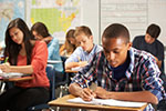 Teens complete written tests while seated at school desks, represents school-based health centers to promote health equity.