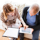 A woman shows an older man how to use a tablet computer.