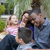 A mom, dad, and two children sit outside of a house.