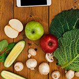 A mobile phone sits on a table near fruits and vegetables.