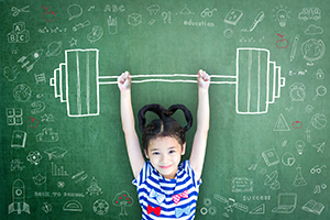 A young girl stands in front of a chalkboard with a barbell drawn on it.