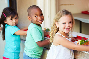 A group of elementary age children getting school lunches.